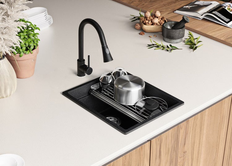 Schwarze Küchenspüle mit Abtropfgestell, Armatur und Geschirr auf einer Küchentheke