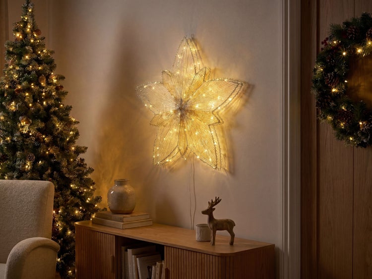 Warm leuchtender LED-Stern an der Wand in einem weihnachtlich dekorierten Raum mit Tannenbaum und Holzsideboard.