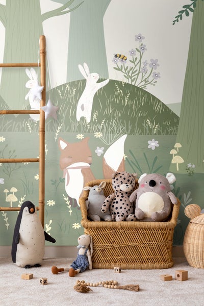 Dekoratives Kinderzimmer mit Waldtapete und Stofftieren in einem geflochtenen Korb