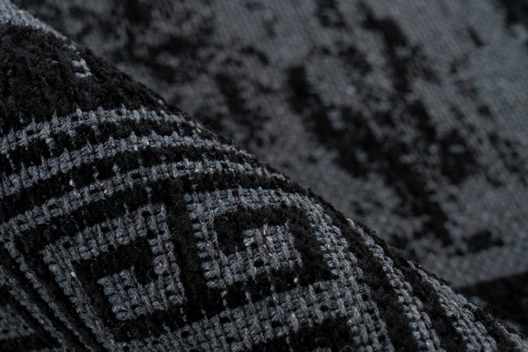 Nahaufnahme eines gewebten Teppichs mit gemustertem Design und umgeschlagener Ecke zur Ansicht der Rückseite und Kantenverarbeitung.