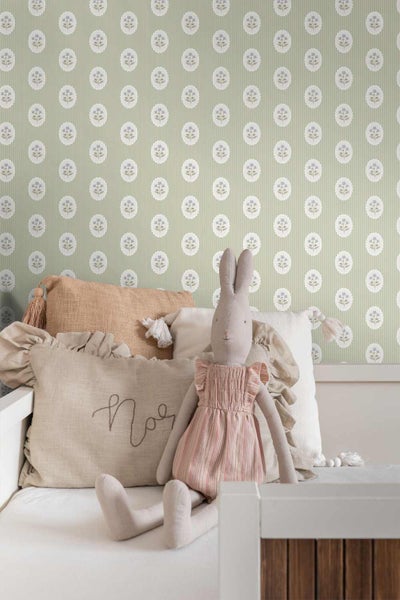 Vliestapete mit Streifenmuster und Blumenmedaillons in einem Kinderzimmer hinter einem weißen Bett mit Kissen und Stoffhase.
