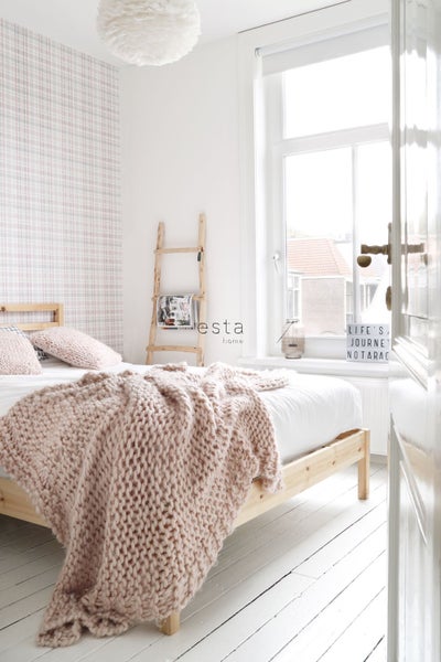 Helles Schlafzimmer mit Holzbett, Strickdecke, Leiterregal und karierter Tapete