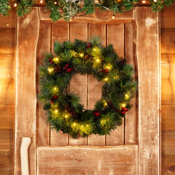 Weihnachtliche Szene mit einem geschmückten Türkranz aus Tannenzweigen, Zapfen und roten Beeren an einer Holztür.