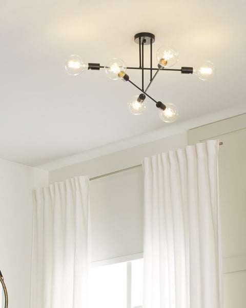 Moderne Deckenleuchte aus schwarzem Metall mit sechs Armen und klaren Glaskugellampen in einem hellen Raum mit weißen Vorhängen.