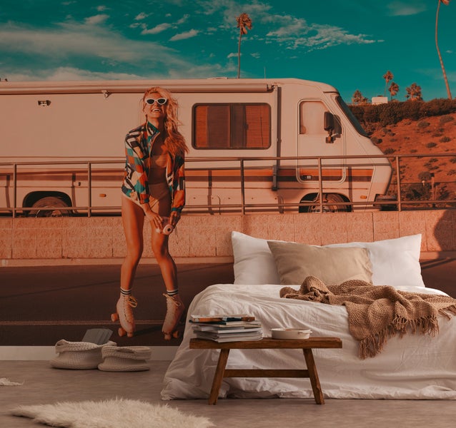 Fototapete mit einer Frau auf Rollschuhen vor einem Wohnmobil in einem Schlafzimmer mit Bett und kleinem Holztisch.