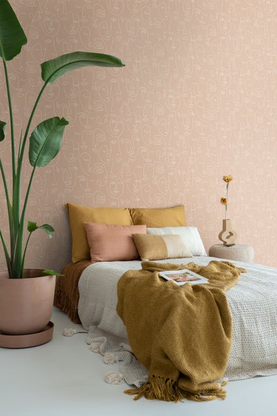 Schlafzimmer mit Bett, Kissen, Tagesdecke und einer Tapete mit Gesichtermuster