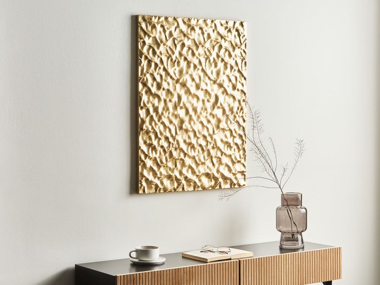 Szene mit einer goldenen Reliefwanddekoration über einem Sideboard mit einem Buch, einer Tasse und einer Vase mit Zweigen