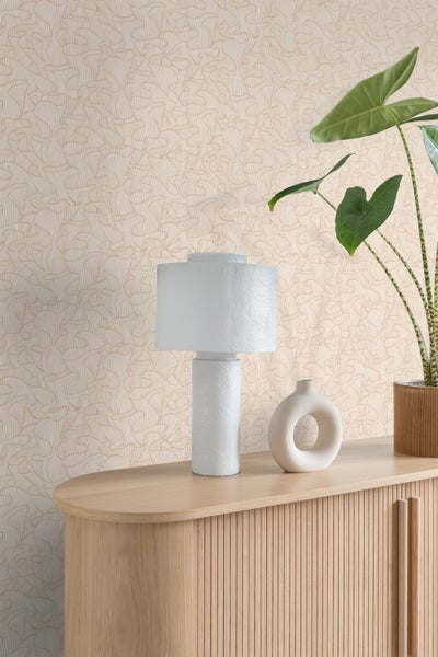 Vliestapete mit abstraktem Wellenmuster hinter einem Sideboard aus Holz mit Lamellenfront, Tischlampe und Zimmerpflanze.