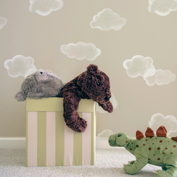 Kinderzimmer mit Wolken-Wandtattoo, gestreifter Aufbewahrungsbox mit Stofftieren und einem Plüsch-Dinosaurier auf dem Teppich.