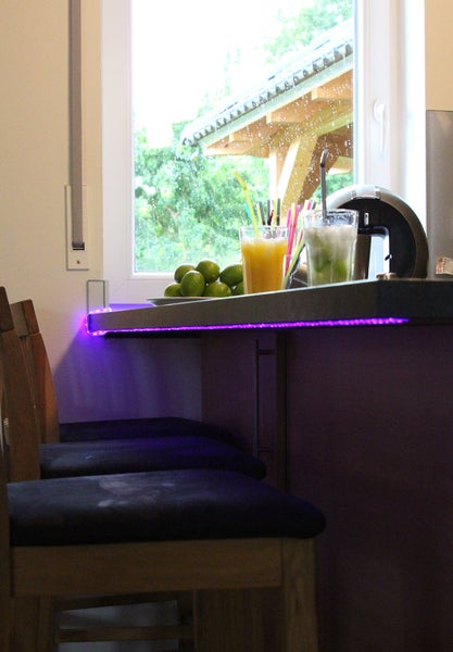 Bar mit Getränken, Limetten und LED-Beleuchtung vor einem Fenster