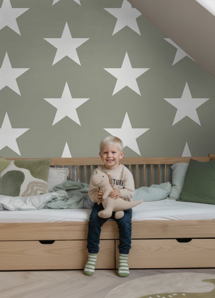 Vliestapete mit großen Sternen in einem hellen Kinderzimmer hinter einem Kinderbett aus Holz.