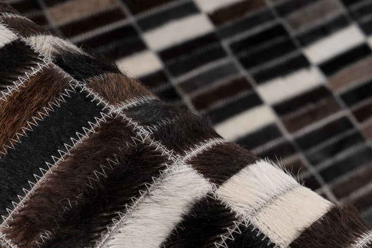 Patchwork-Teppich aus Kuhfell-Rechtecken mit Zickzack-Naht und grauer Filz-Rückseite.