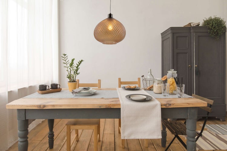 Esstisch mit Geschirr, Tischläufer, Hängeleuchte und Dekoration in einem Esszimmer.