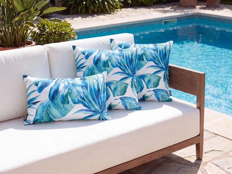 Gartensofa mit Kissen mit Blattmuster auf einer Terrasse vor einem Pool.