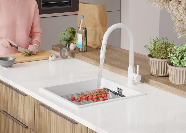 Küchenszene mit weißer Spüle, Armatur und Frau, die Gemüse schneidet