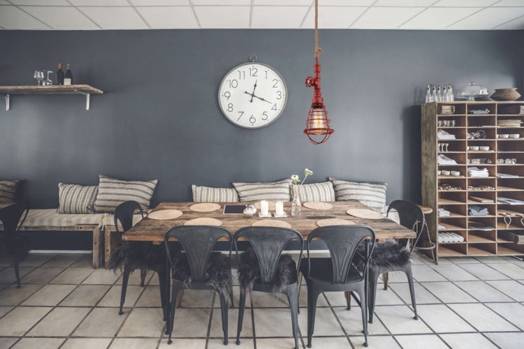 Innenaufnahme eines Esszimmers mit Holztisch, Stühlen, Wanduhr und Regalen.