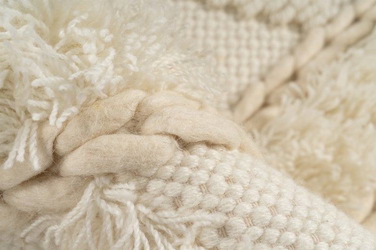 Nahaufnahme der Textur eines gewebten Teppichs mit geflochtenen Elementen, Fransen und Noppenmuster.