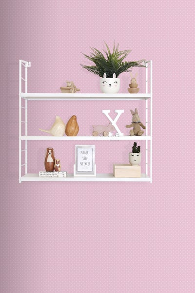 Wandregal mit Dekoration und Zimmerpflanzen vor einer rosa gepunkteten Tapete.