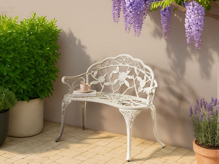 Verzierter Gartenbank aus Metall mit Buch und Tasse, umgeben von Pflanzen.