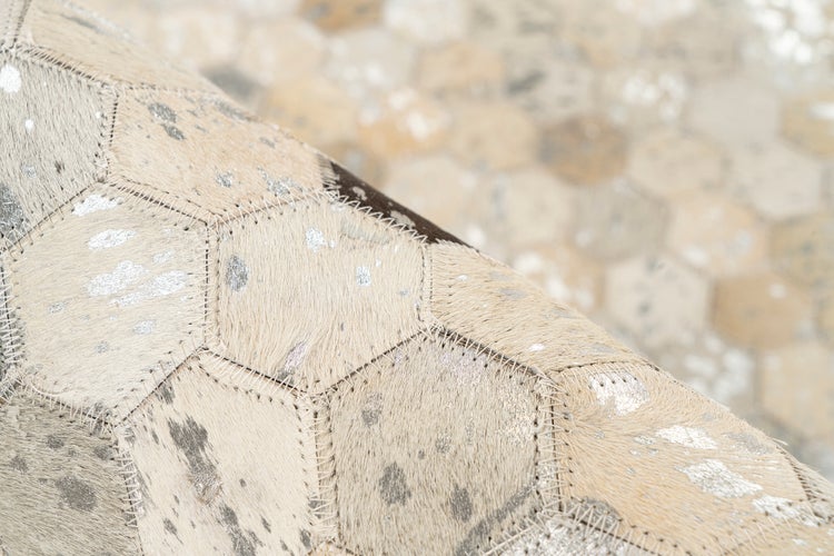 Kuhfellteppich mit hexagonalen Flicken, silbernen Metallic-Akzenten und sichtbaren Nähten.