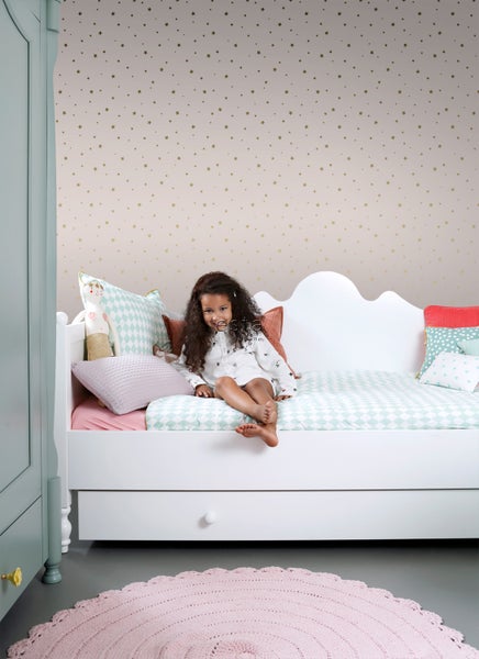 Kinderzimmer mit Mädchen auf einem Bett vor einer Wand mit Sternenmuster