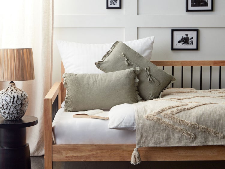 Gemütliche Schlafzimmerszene mit Holzbett, Kissen und dekorativer Tagesdecke