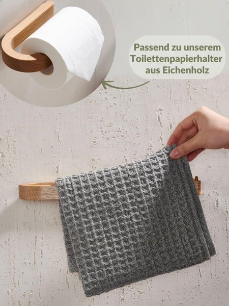 Hand hängt graues Waffelhandtuch an Handtuchhalter aus Eichenholz neben passendem Toilettenpapierhalter aus Eichenholz.