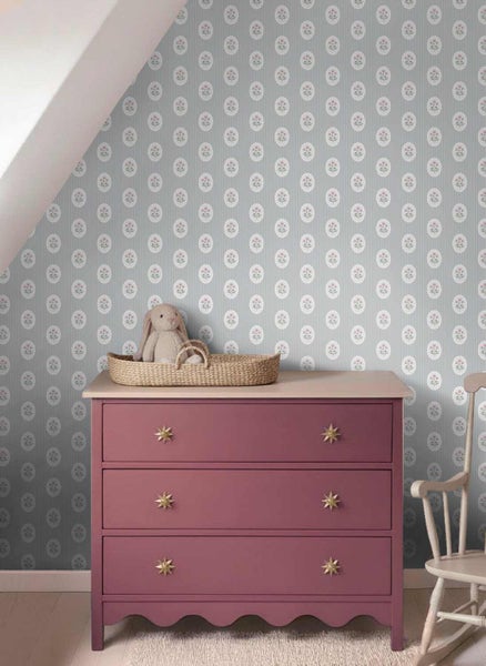 Kinderzimmer mit rosa Kommode und Tapete mit Blumen-Medaillons und Streifen. Ein Stoffhase sitzt in einem Korb auf der Kommode.