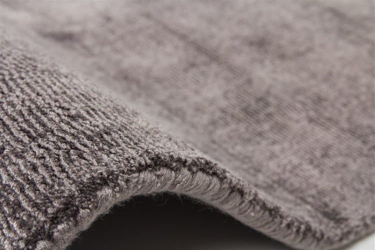 Detailaufnahme eines grauen Teppichs mit strukturierter Oberfläche und sichtbarer Rückseite.