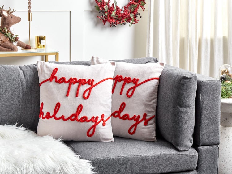 Zwei Kissen mit der Aufschrift 'Happy Holidays' auf einem grauen Sofa in einem Wohnzimmer.