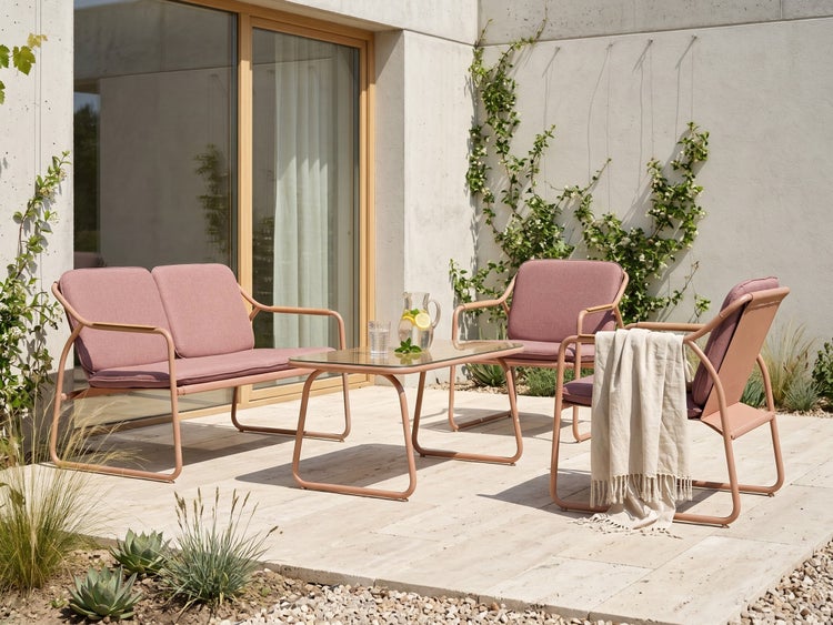 Modernes Garten-Lounge-Set mit Zweisitzer-Sofa, zwei Sesseln und Couchtisch mit Glasplatte auf einer hellen Steinterrasse mit Kletterpflanzen.