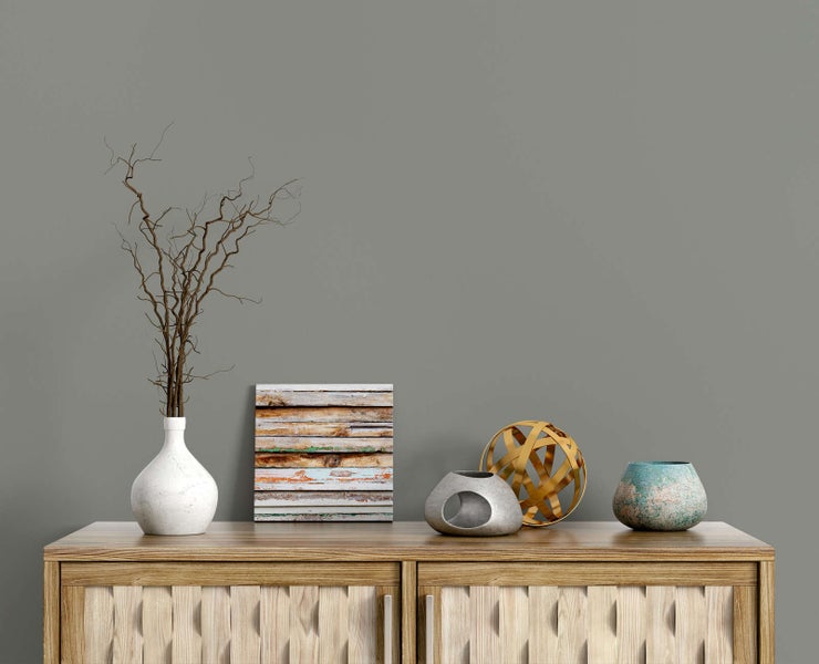 Modernes Sideboard aus Holz vor grauer Wand mit Dekoration aus einer weißen Vase mit Zweigen, einem Holzbild und verschiedenen Objekten.