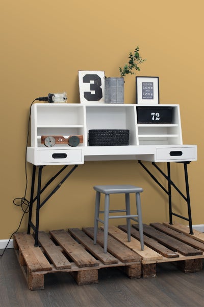 Schreibtisch mit Ablagefächern, Schubladen und Metallbeinen, kombiniert mit einem grauen Hocker auf einer Holzpalette.