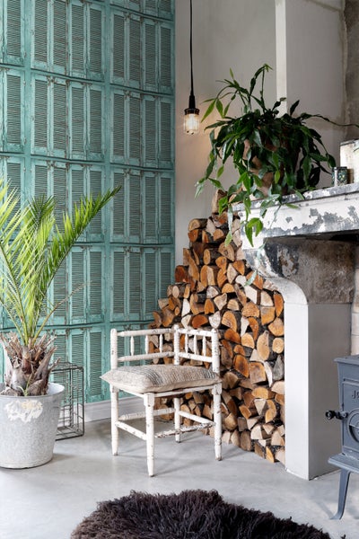 Wohnraum mit dekorativer Wandgestaltung, Holzstapel und Zimmerpflanzen für gemütliche Atmosphäre