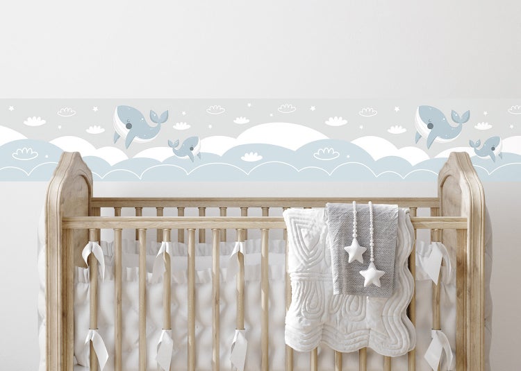 Helle Kinderzimmerszene mit einer gemusterten Bordüre mit Walen und Wolken an der Wand über einem hölzernen Babybett.