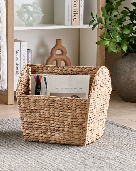 Dekoratives Korbgefäß aus Naturfasern mit Büchern im Wohnzimmerregal.