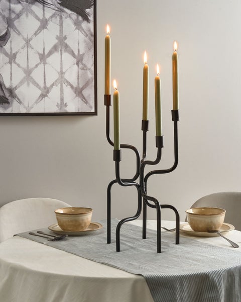 Dekoratives Arrangement mit Kerzenständer aus Metall, Tafelkerzen, Geschirr und Tischdeko auf einem Esstisch.