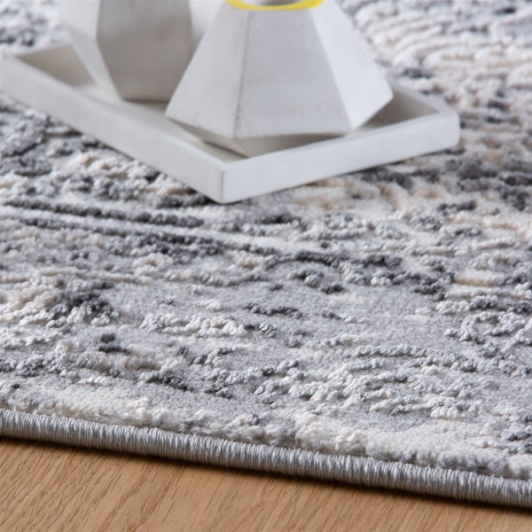 Nahaufnahme eines strukturierten Teppichs mit abstraktem grau-weißem Muster, geketteltem Rand und Hoch-Tief-Struktur auf einem Holzboden.