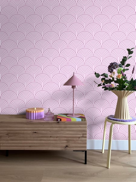 Zimmeransicht mit rosafarbener Retro-Tapete, Kommode, Tischlampe, Blumen und Hocker