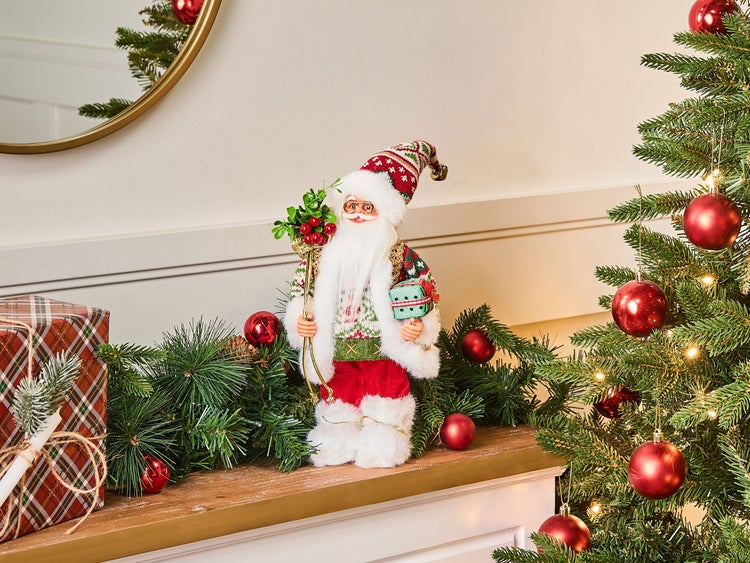 Dekorativer Weihnachtsmann auf einem Kaminsims mit Weihnachtsbaum und Geschenk