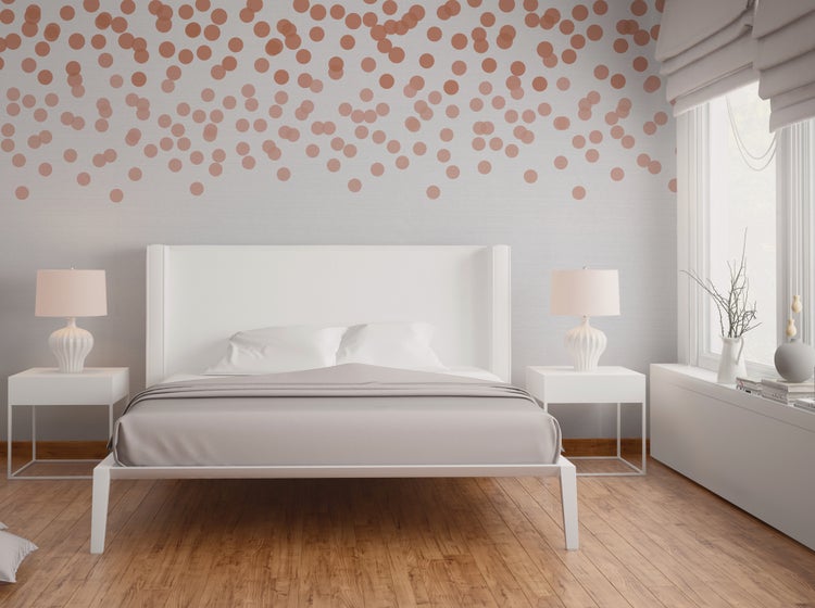 Modernes Schlafzimmer mit weißem Bett, Nachtkonsolen und kupferfarbenen runden Wandtattoos auf einer hellen Wand über Parkettboden.