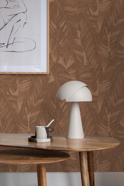 Moderne Tischleuchte mit pilzfoermigem Schirm auf einem Holztisch mit Tasse vor gemusterter Tapete.