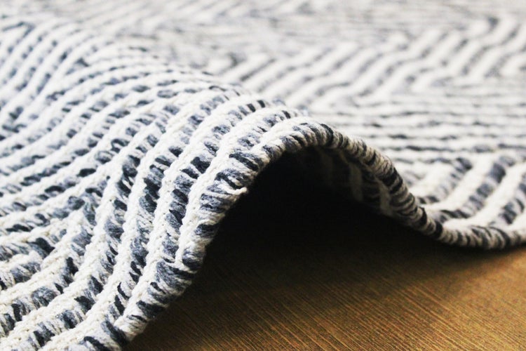 Gewebter Teppich mit schwarz-weißem Zickzack-Muster, Nahaufnahme der Textur auf Holzboden.