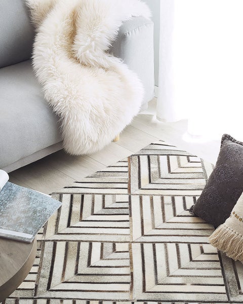 Szene mit einem Sofa, einem Fell, Kissen und einem Teppich mit geometrischem Muster.