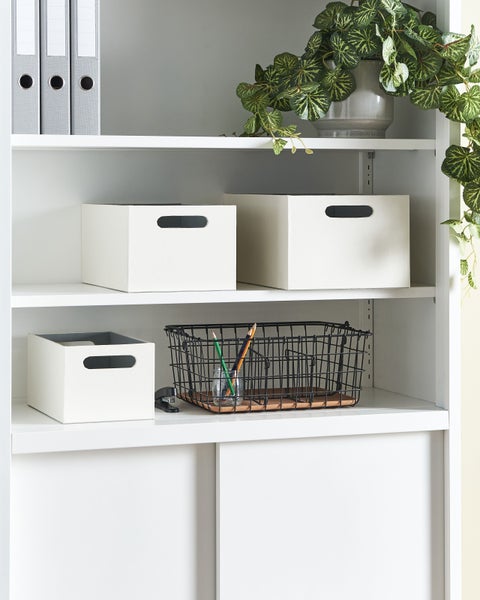 Ein weißes Regal mit Ordnern, Aufbewahrungsboxen, einer Pflanze und einem Drahtkorb für Bürobedarf.