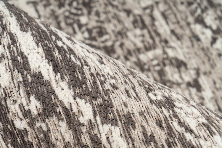 Detailansicht eines Teppichs mit abstrakter Musterung und umgeklappter Ecke, die die dunkle Rückseite zeigt.