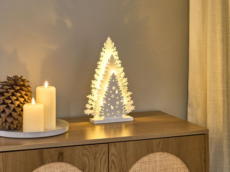 Dekoratives Arrangement mit beleuchtetem Weihnachtsbaum aus Holz, Kerzen und Tannenzapfen auf einem Holzschrank