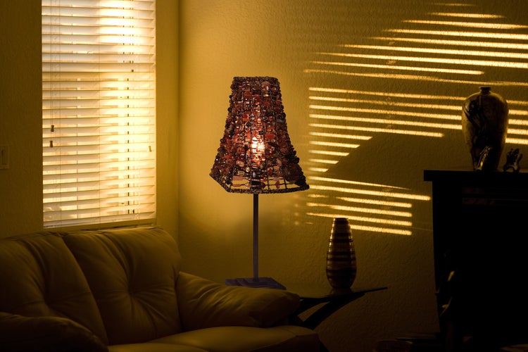 Dekorative Tischleuchte mit Lampenschirm aus Schmucksteinen auf einem Tisch mit Zimmerpflanze und Uhr