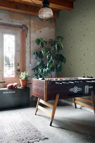 Zimmer mit Fußballtapete, Tisch, zwei Hockern, Pflanze und Dinosaurierfigur