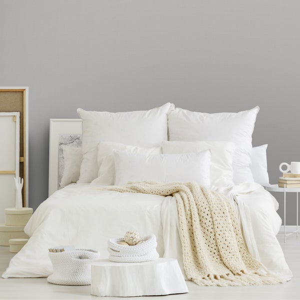 Helles Schlafzimmer mit einem Bett, weißer Bettwäsche, mehreren Kissen und einer grob gestrickten Wohndecke.